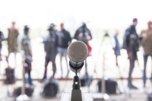 Microphone in focus against blurred camera operators and reporters at conference